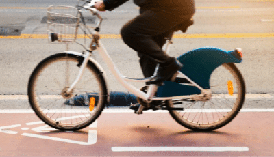 Une personne conduisant un vélo blanc avec un panier avant et un garde-boue arrière bleu sur une piste cyclable désignée près d'une rue, capturée en mouvement - une scène idéale pour les ateliers et formations risques routiers axés sur la sécurité à vélo en milieu urbain.